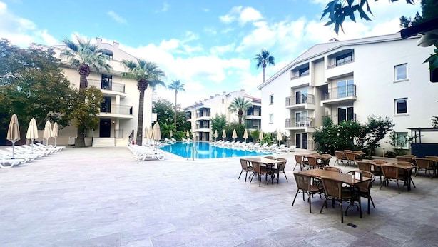 Zwembadgedeelte van een resort met ligbedden en parasols, omringd door meerlaagsgebouwen met balkons.