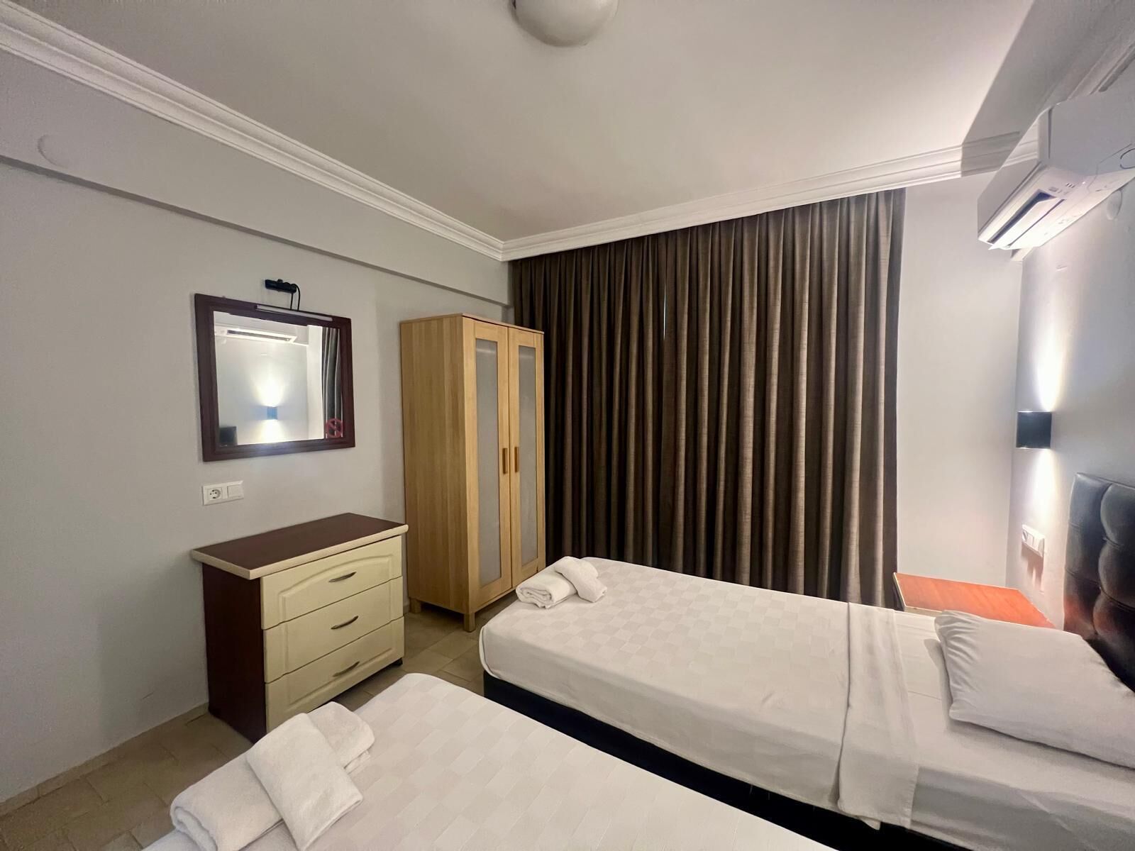Ein Hotelzimmer mit zwei Betten, einem Schrank, einem Spiegel und einem Fenster mit Vorhängen.
