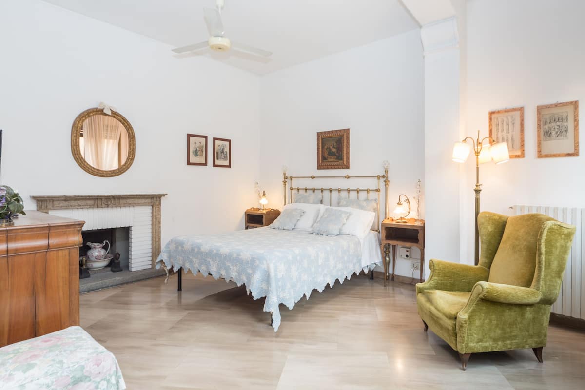 Een slaapkamer met een bed, een stoel, een open haard en ingelijste foto's aan de muur.