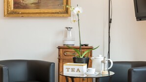 A room with a table displaying a tea set, a potted orchid, and a framed painting on the wall.