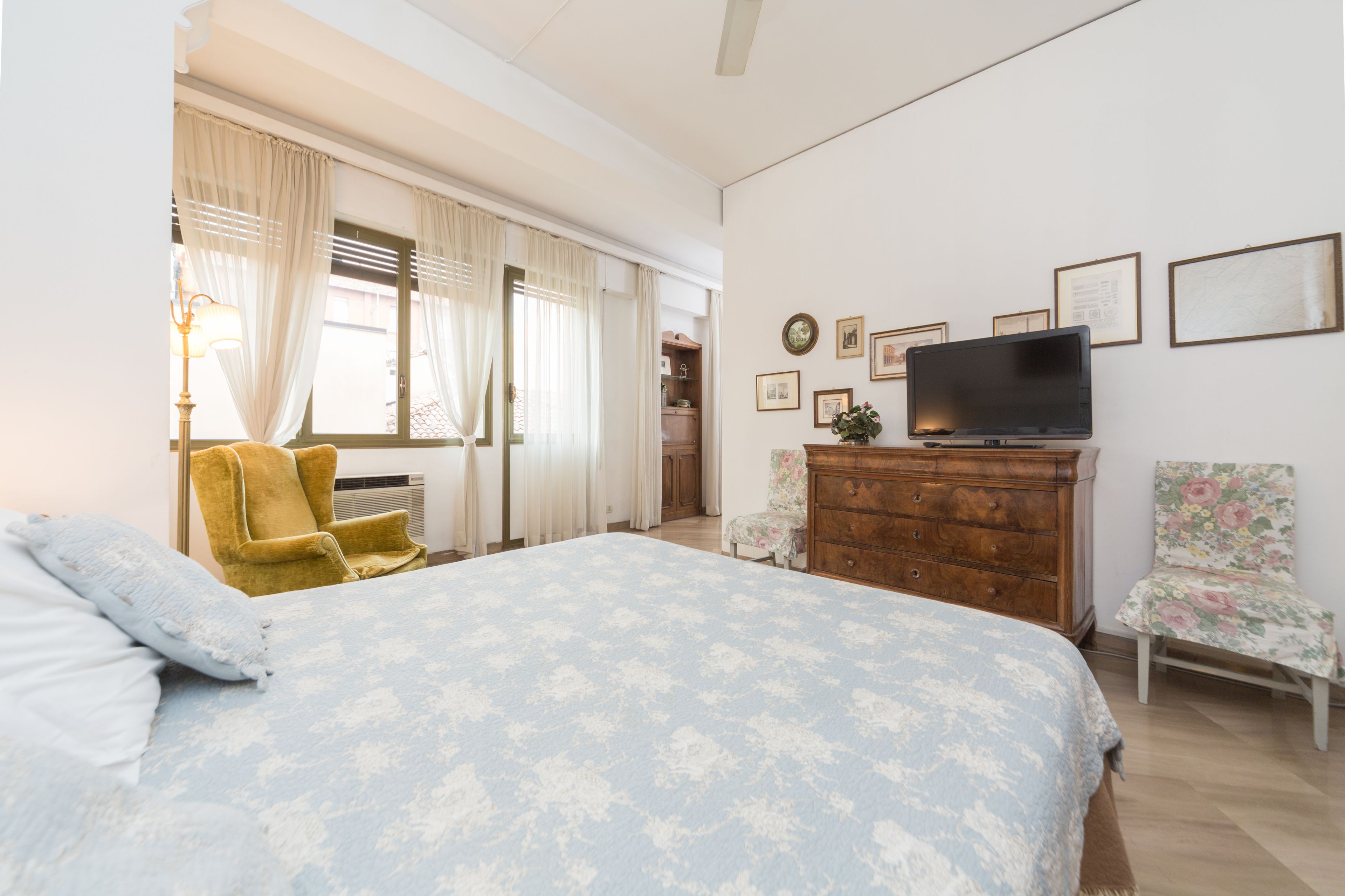 Een slaapkamer met een bed, een dressoir, een televisie en twee stoelen.
