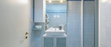 Een badkamer met een wit wastafel, spiegel en douchehoek.