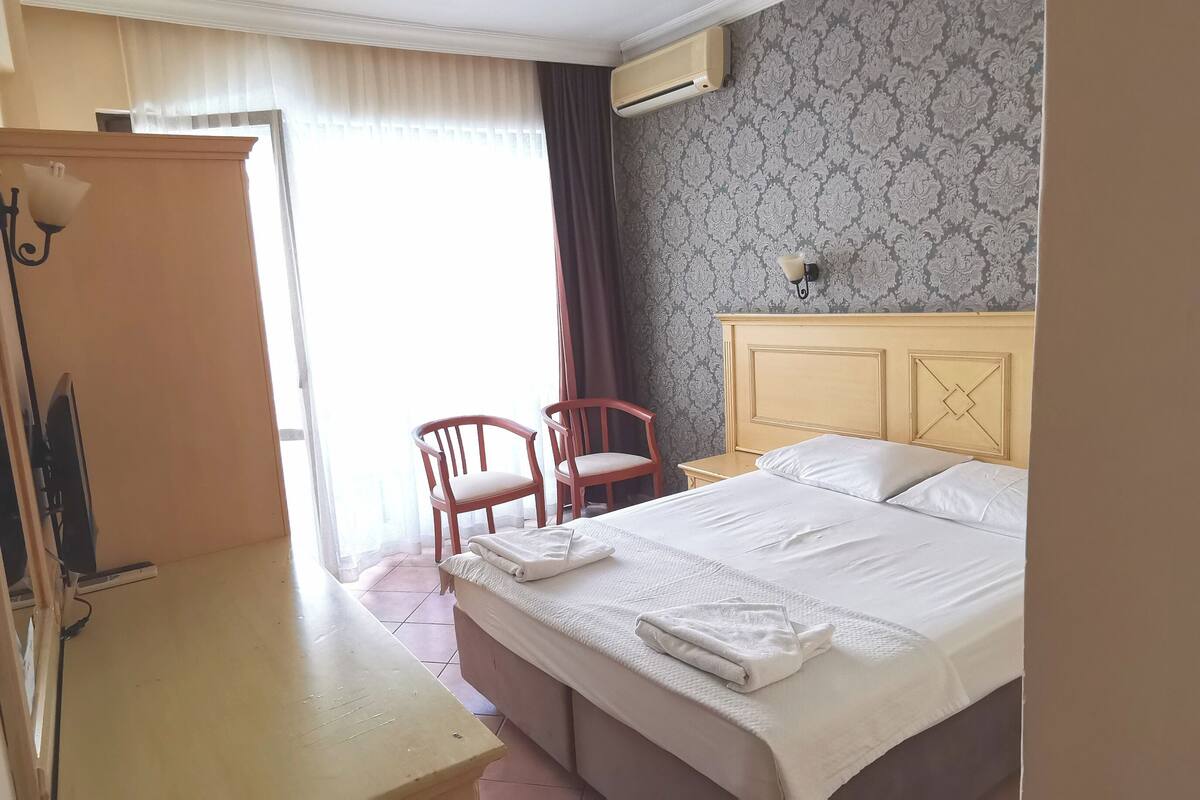 Quarto de hotel com cama, cadeira, escrivaninha e guarda-roupa.
