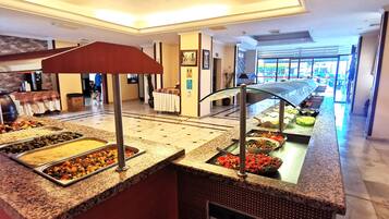 A buffet area with various food options, a glass partition, and a view of the hotel lobby.