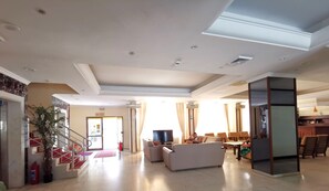 Amplia sala de estar con televisor de pantalla plana, sofás, una mesa de comedor y una escalera con alfombra roja.