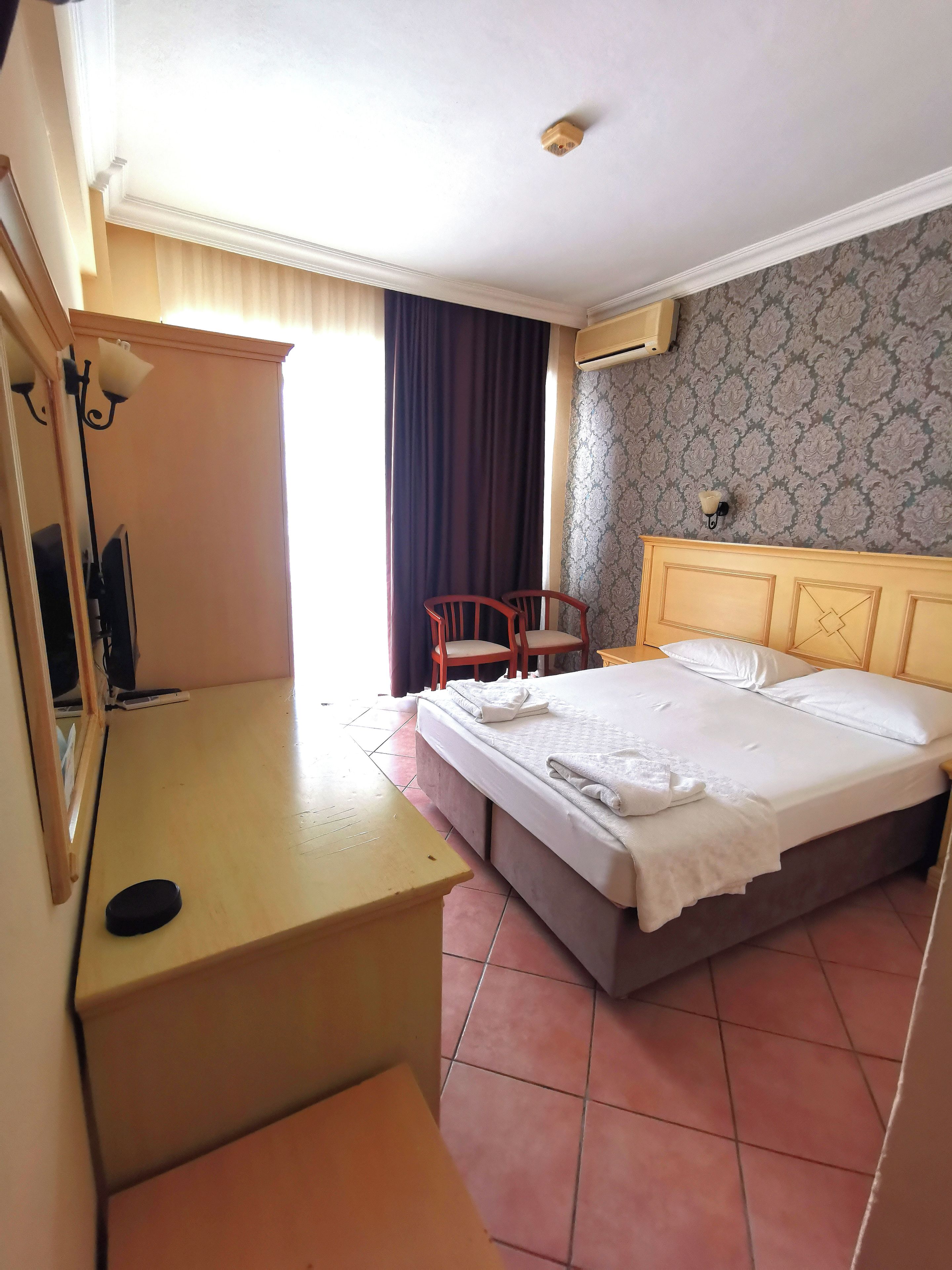 A hotel room with a bed, a desk, a chair, a mirror, and a window with curtains.
