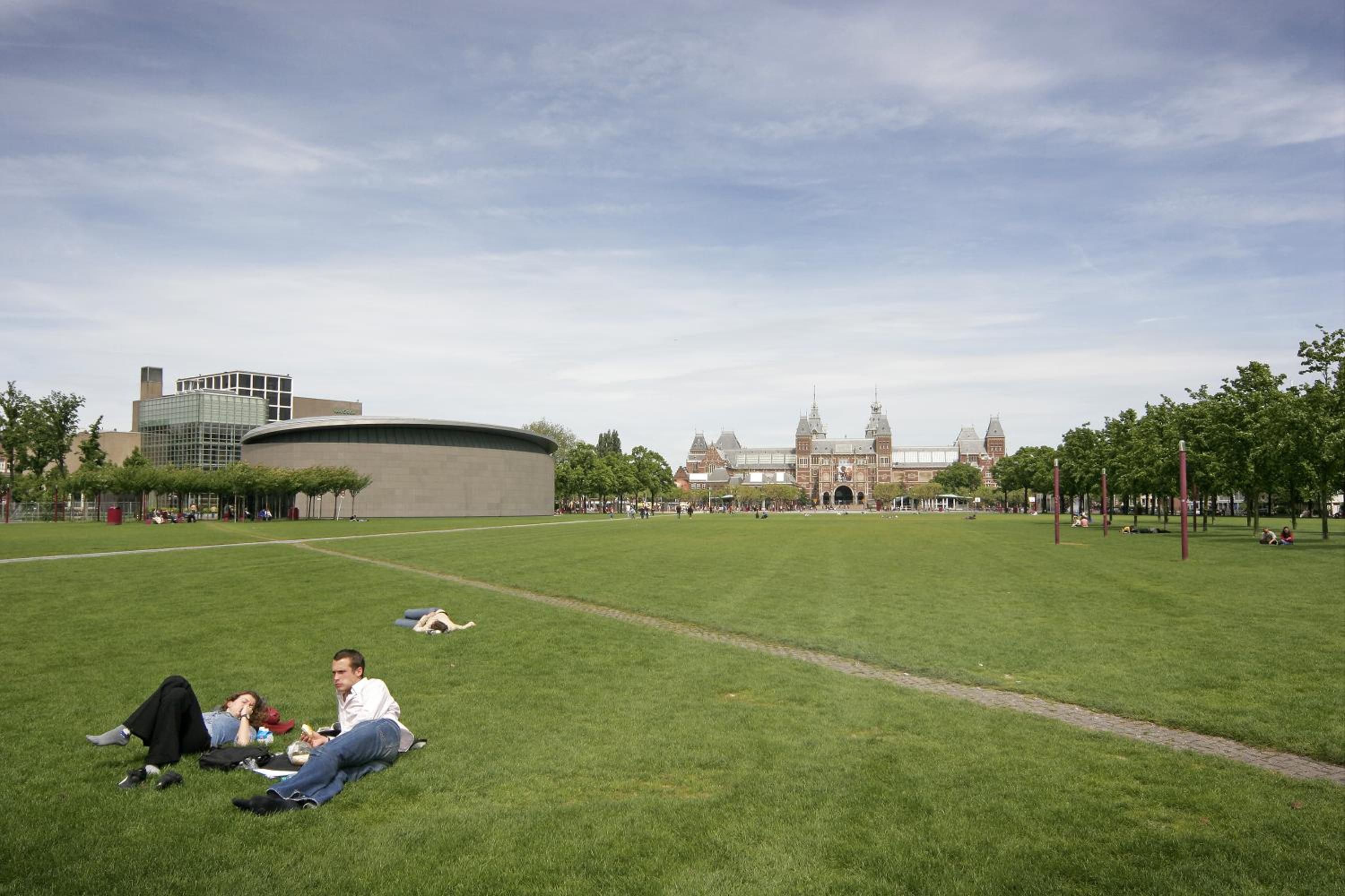 Un parque con césped, un edificio moderno y otro histórico al fondo.