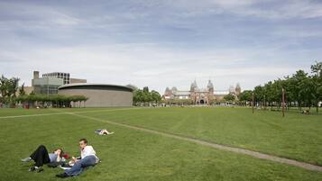 Un parque con césped, un edificio moderno y otro histórico al fondo.