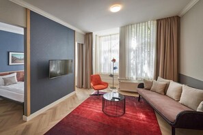 A hotel room with a bed, a sofa, a red rug, a TV, and a window with curtains. - Nova Apartments (Amsterdam)