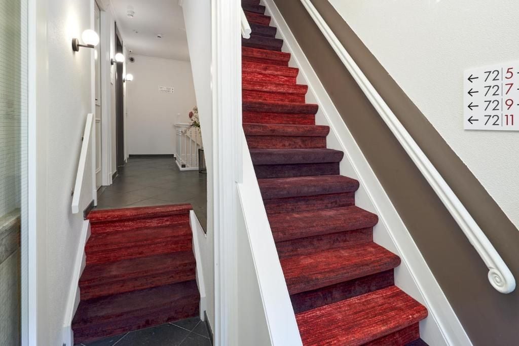 Una escalera con peldaños cubiertos de alfombra roja y barandilla blanca, que conduce a un rellano con un letrero con números.