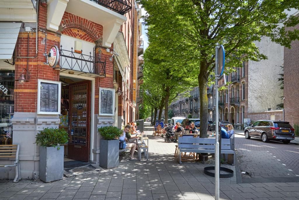 Une rue avec des terrasses, un bâtiment en briques et des voitures garées.