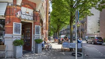 Une rue avec des terrasses, un bâtiment en briques et des voitures garées.