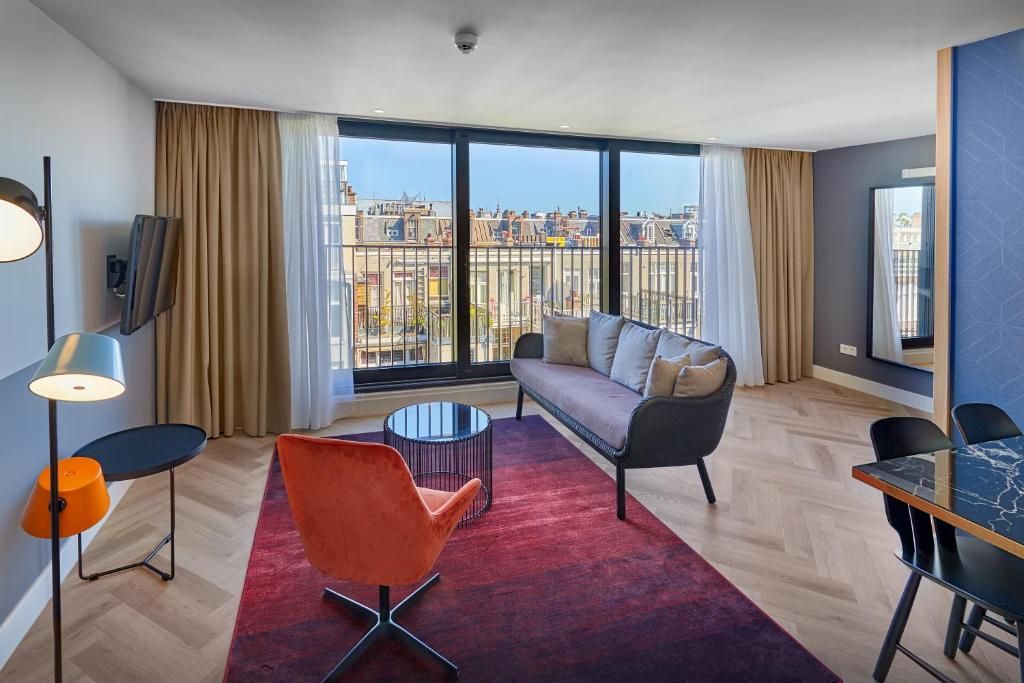 A modern hotel room with a sofa, armchair, and dining table.