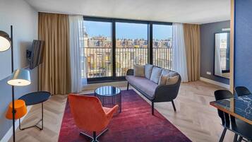 A modern hotel room with a sofa, armchair, and dining table.