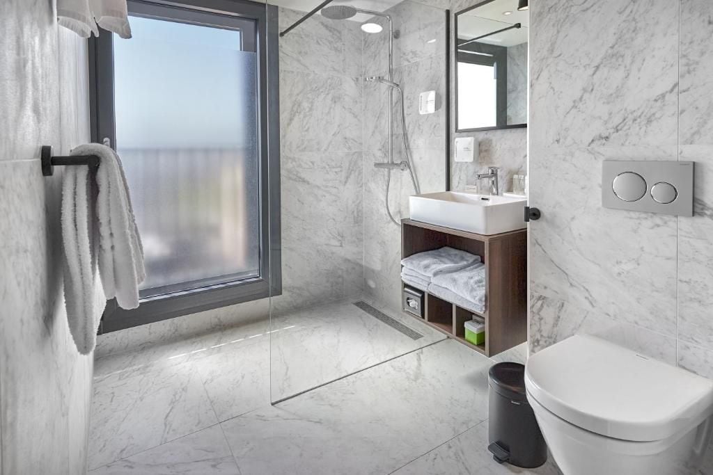 Un baño moderno con un ventanal grande, una ducha, un lavamanos y un inodoro.