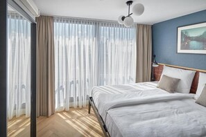 A bedroom with a bed, curtains, a nightstand, a lamp, and a painting on the wall. - Nova Apartments (Amsterdam)
