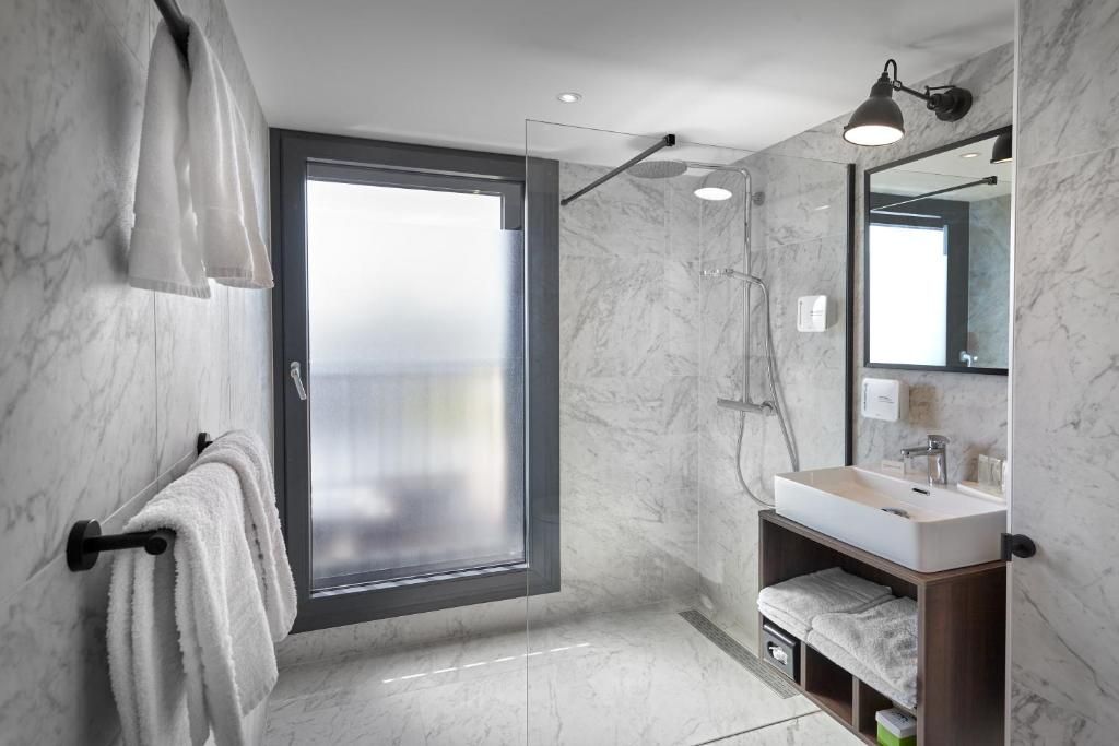 Un baño moderno con mampara de vidrio, un lavamanos con espejo y toallas en un perchero.