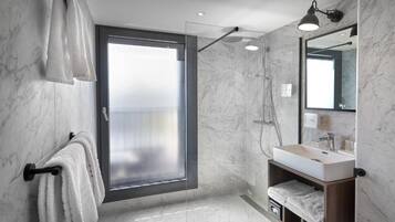 Un baño moderno con mampara de vidrio, un lavamanos con espejo y toallas en un perchero.