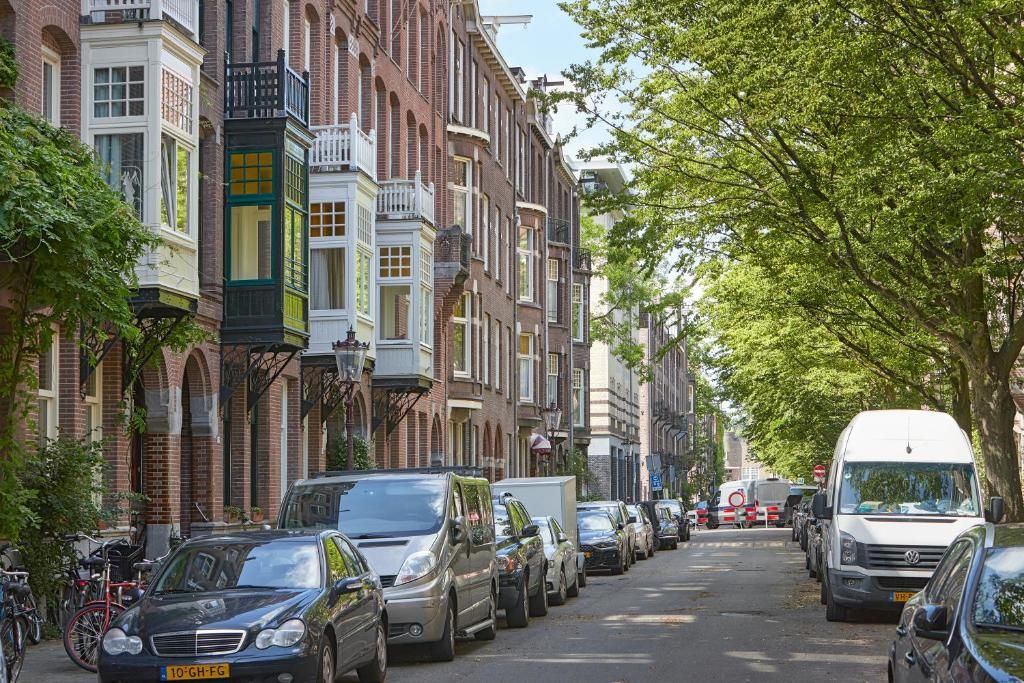 Een straat met geparkeerde auto's en traditionele bakstenen gebouwen met erkers.
