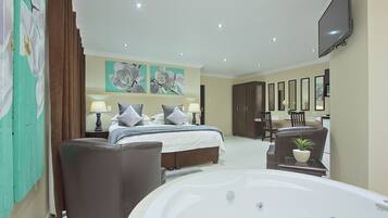 A modern hotel room with a large bed, a sitting area with a chair, a desk, a TV, and a large bathtub.