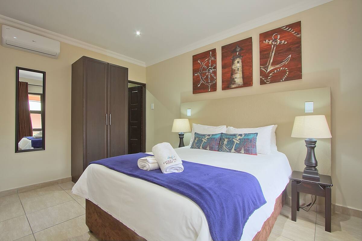 A hotel room with a bed, two bedside lamps, a wardrobe, and artwork on the wall.