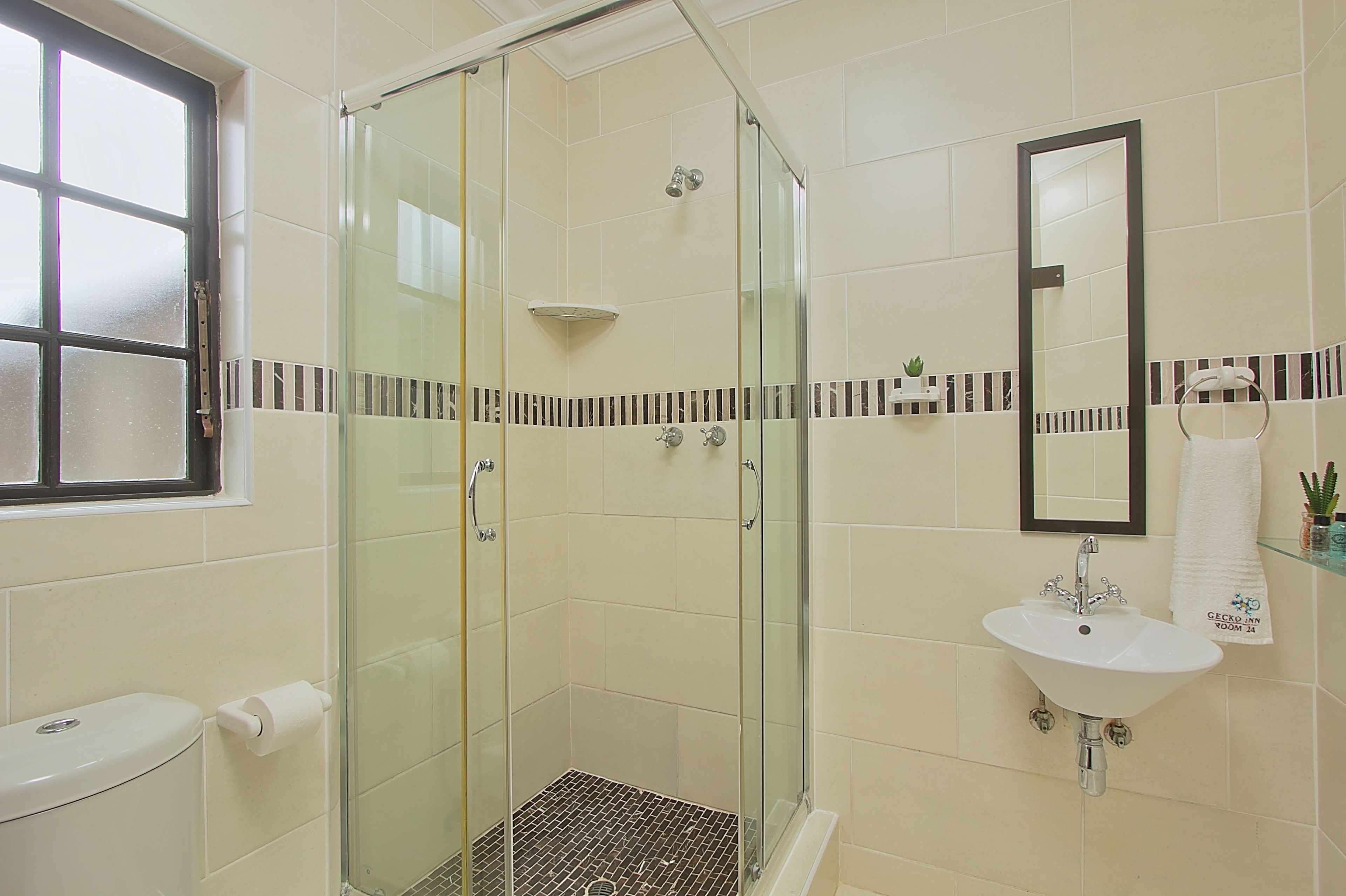A bathroom with a glass-enclosed shower, a toilet, and a sink with a mirror above it.