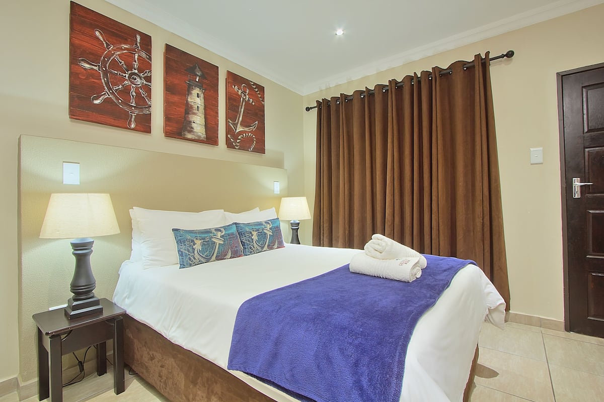 A neatly made bed with a blue blanket, two bedside lamps, and decorative wall art.