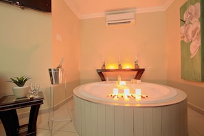 A bathroom with a round bathtub, a potted plant, a table with glasses, and a wall-mounted air conditioner. - Gecko Inn Guest House (Richards Bay)