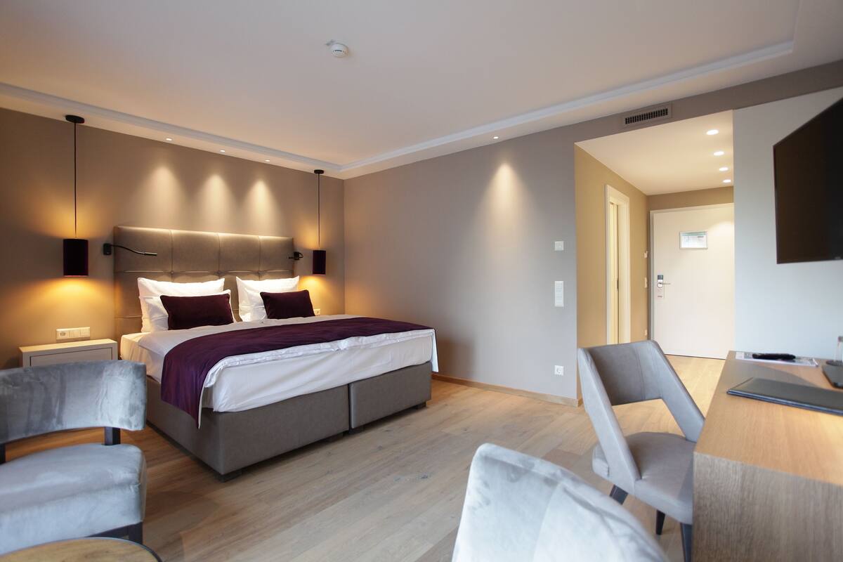 A modern hotel room with a large bed, bedside tables, a desk, and a chair.