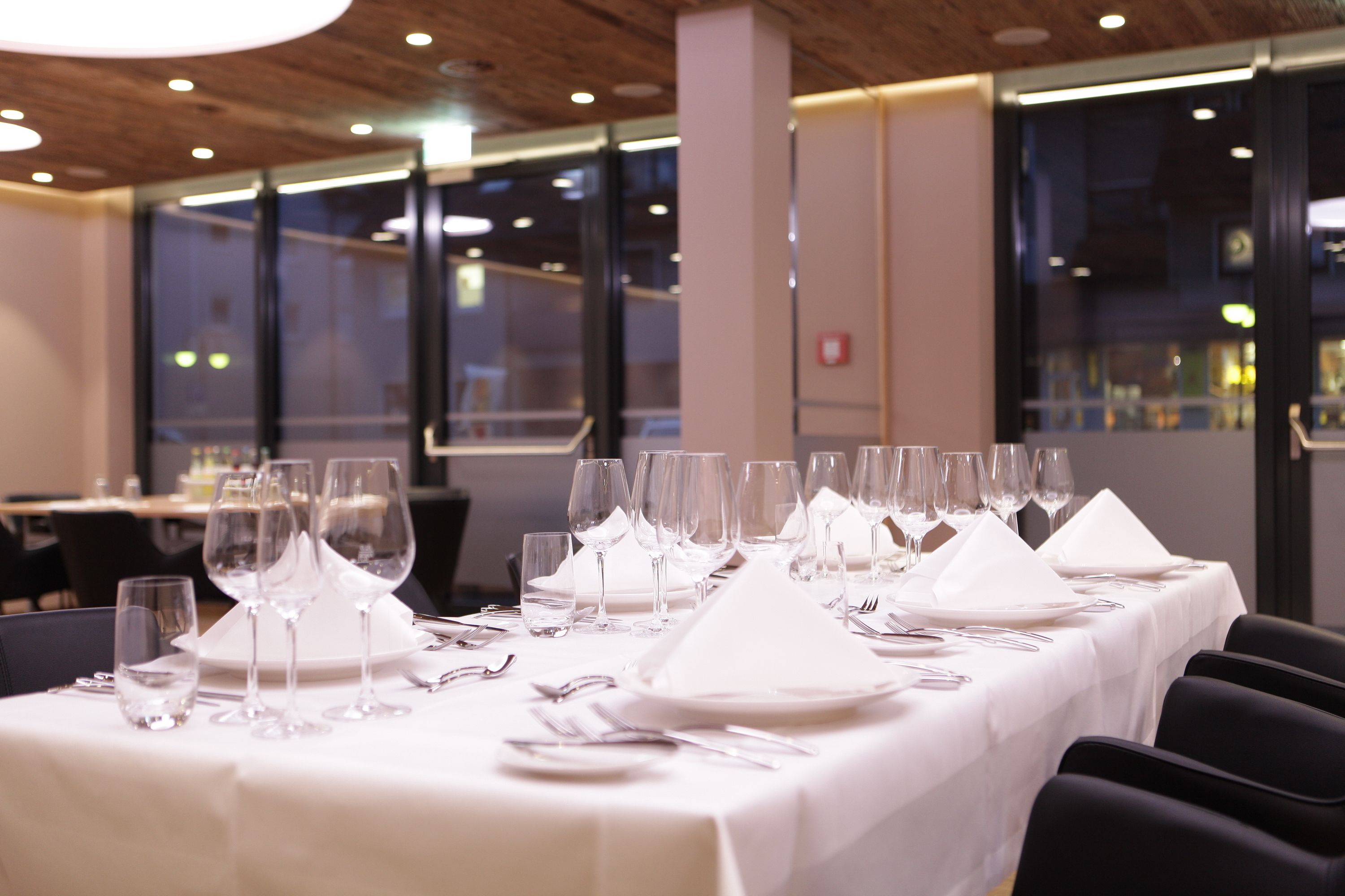 A restaurant with a long table set for a formal meal, featuring multiple wine glasses and plates.