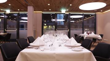 A dining area with tables set for a meal, featuring white tablecloths, black chairs, and a modern ceiling design.
