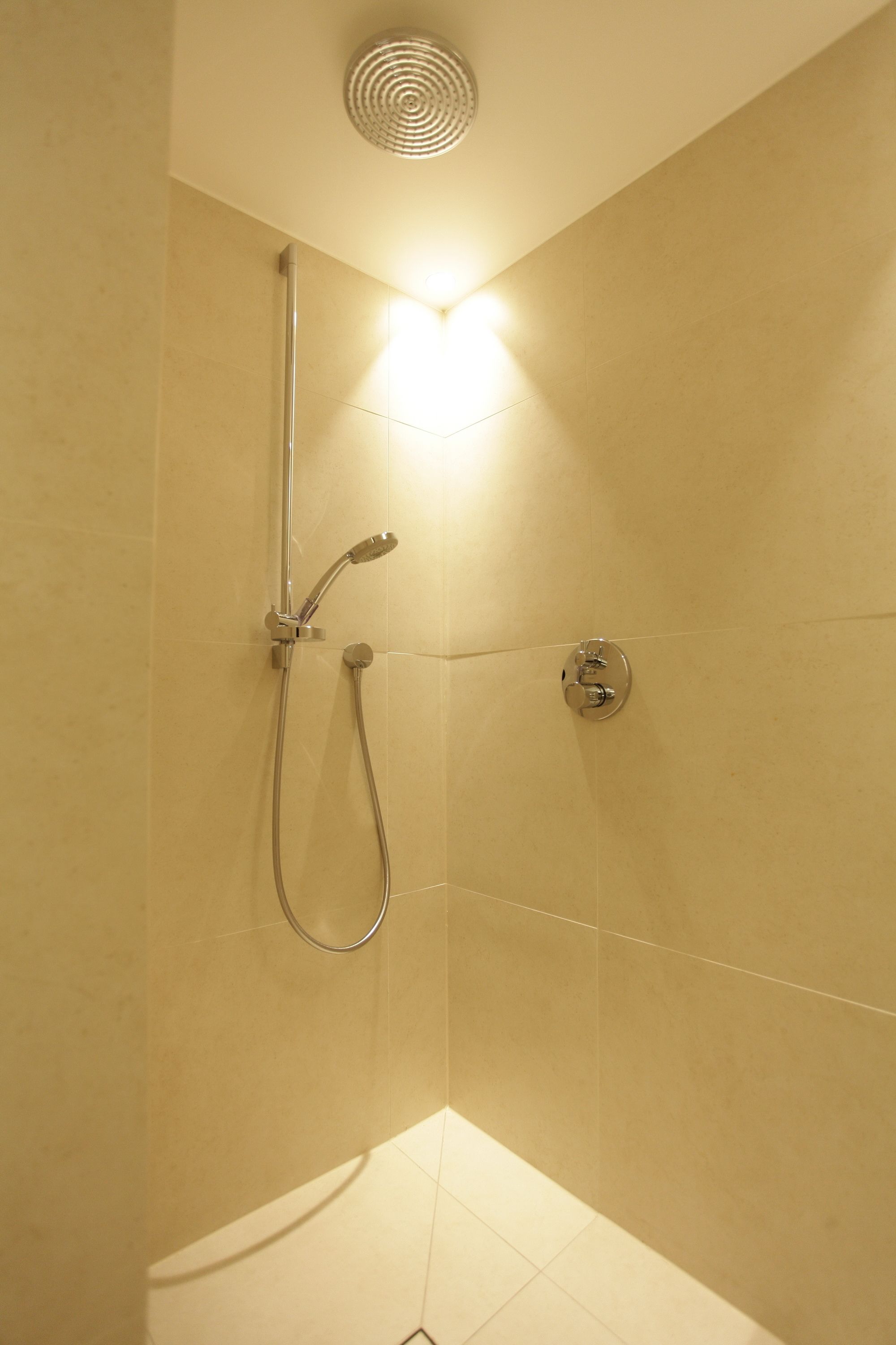 Eine Eckdusche mit Handbrause und am Wand montiertem Wasserhahn.