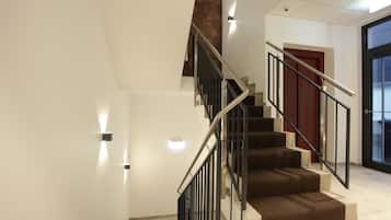 Una escalera moderna con barandas metálicas y peldaños alfombrados, que conduce a una habitación con puerta de vidrio y una pared de acento roja.