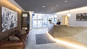 A modern hotel lobby with a reception desk, a leather sofa, and artwork on the walls. - Hotel Aurelia (Aldingen)