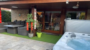 An outdoor patio area with a hot tub, wicker furniture, and potted plants. - B&B Kookhai (Kluisbergen)