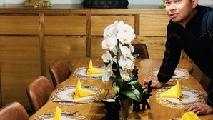 A dining table set with yellow napkins, white flowers, and a metal cup. - B&B Kookhai (Kluisbergen)
