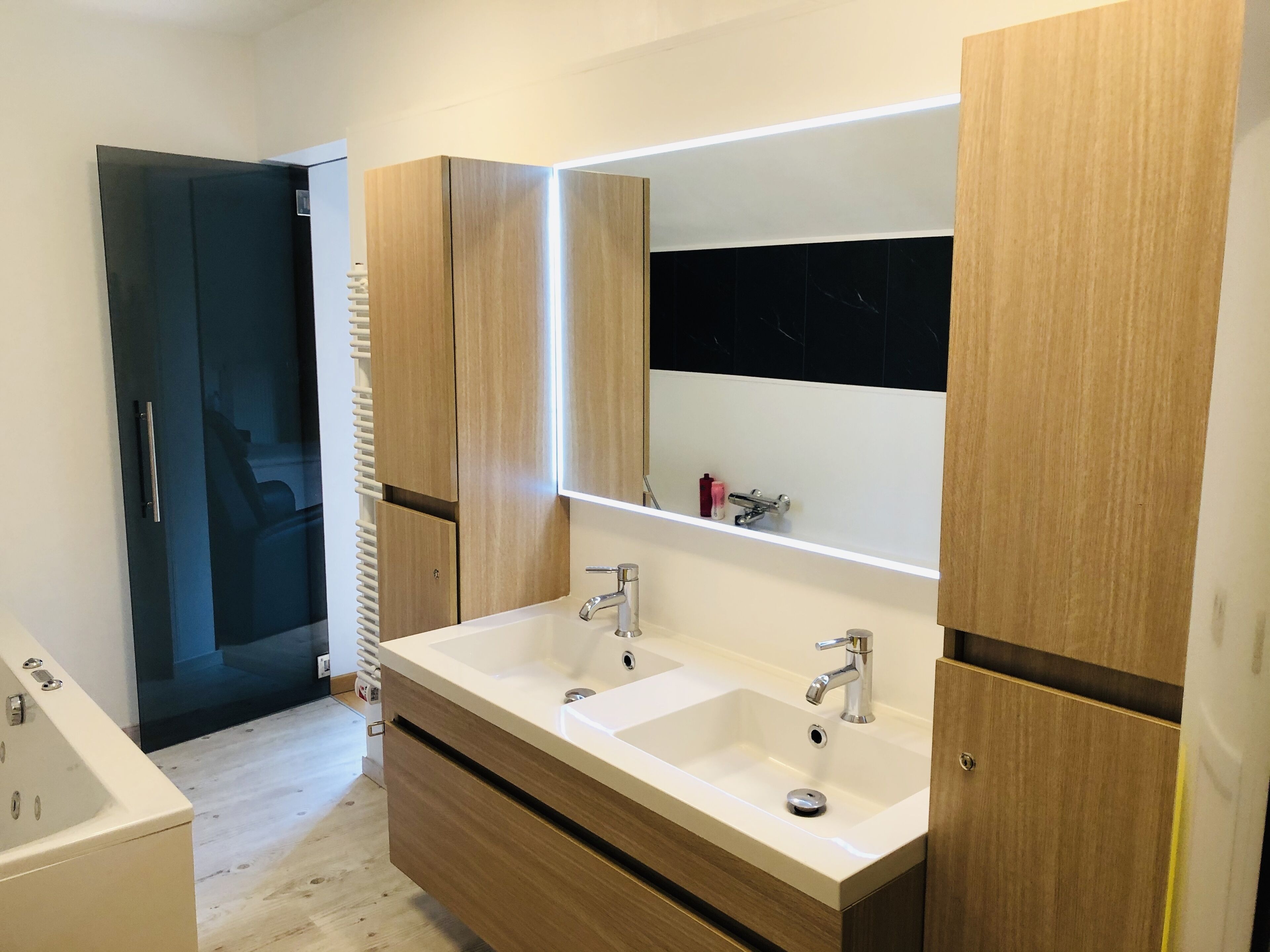 A modern bathroom with two sinks, a large mirror, and wooden cabinetry.