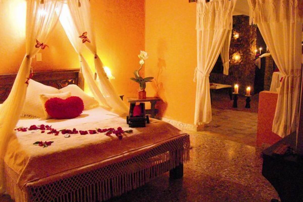 A room with a bed, a nightstand, and a chair. There are candles on the floor.