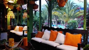A cozy outdoor seating area with cushioned benches and orange cushions, surrounded by lush greenery and a view of a pool. - Hotel Iguaque Campestre Spa & Ecolodge (Villa de Leyva)