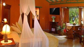 A bedroom with a bed under a canopy, a bedside table with a lamp, a TV on the wall, and a dining area with a table and chairs. - Hotel Iguaque Campestre Spa & Ecolodge (Villa de Leyva)