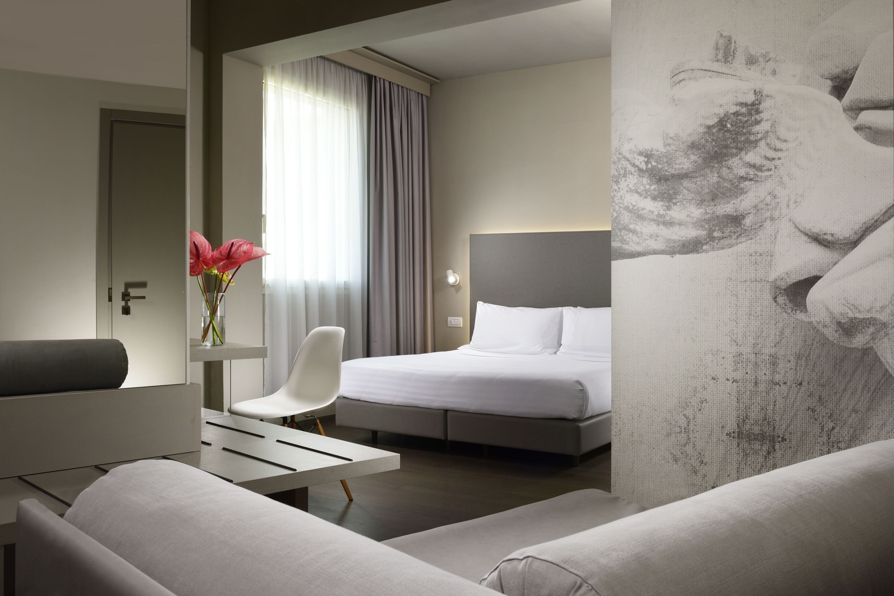 A modern hotel room with a bed, a desk, a chair, and a large painting on the wall.