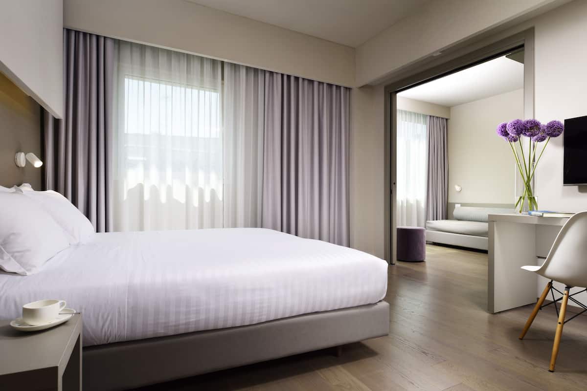 Een moderne hotelkamer met een groot bed, een bureau en een stoel. Er is een televisie aan de muur bevestigd en een raam met gordijnen.
