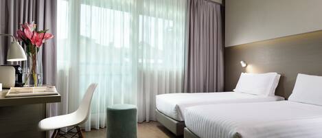 A hotel room with two beds, a desk with a lamp, a chair, and a small ottoman.