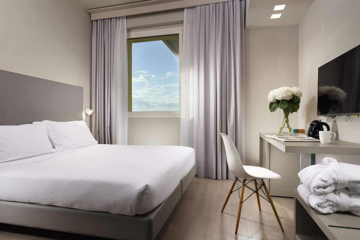 Een moderne hotelkamer met een groot bed, een bureau met stoel, een flatscreen televisie en een raam met gordijnen.