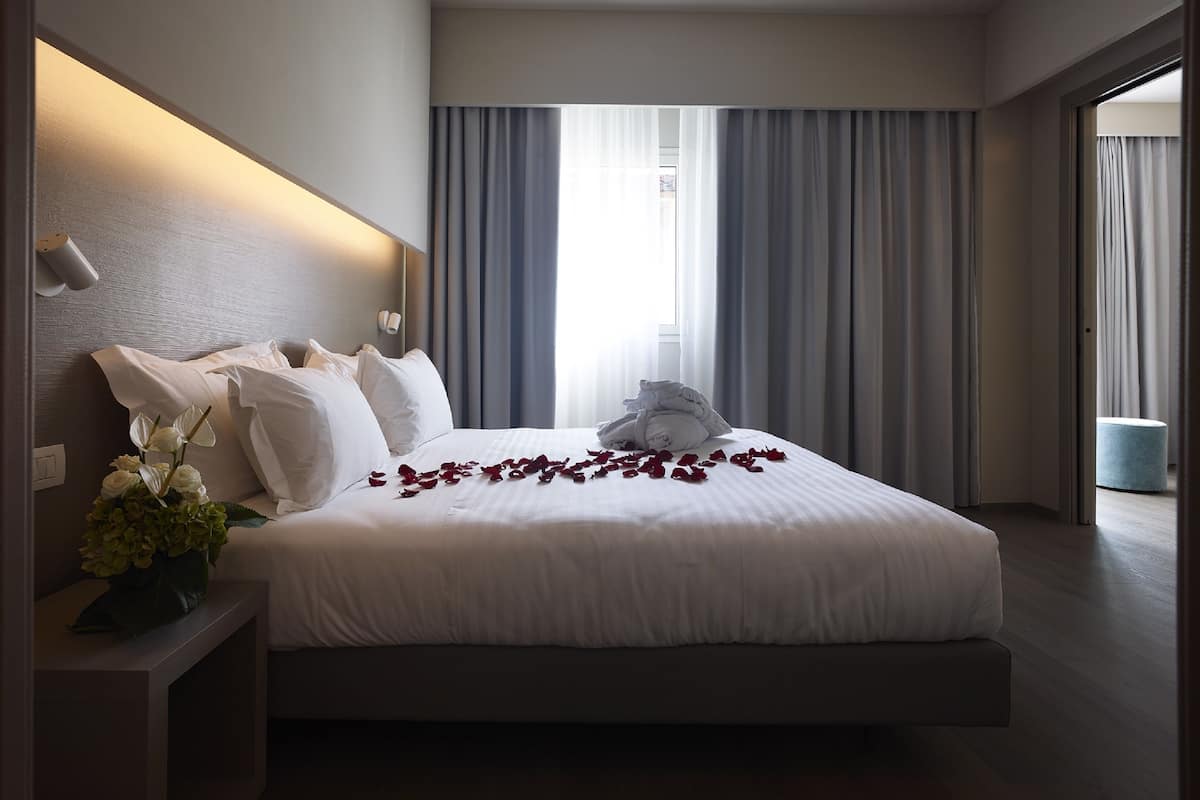 Een moderne hotelkamer met een groot bed, een nachtkastje met een bloemenvaas, en uitzicht op het omliggende landschap door grote ramen.