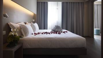 Habitación de hotel moderna con una cama grande, una mesita de noche con un jarrón de flores y vistas al exterior a través de amplios ventanales.