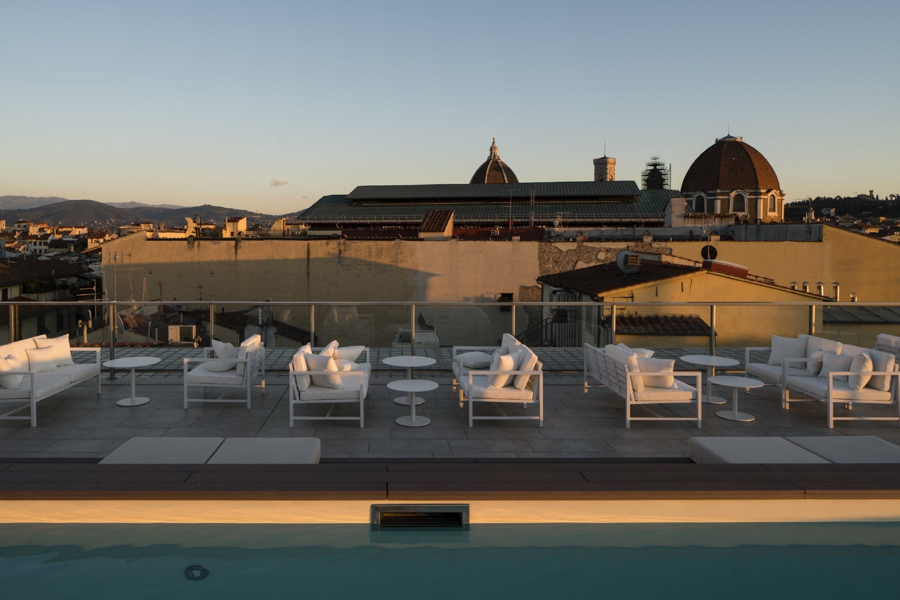 A rooftop pool area with white lounge chairs and tables, a clear view of a historic building with a dome in the background.