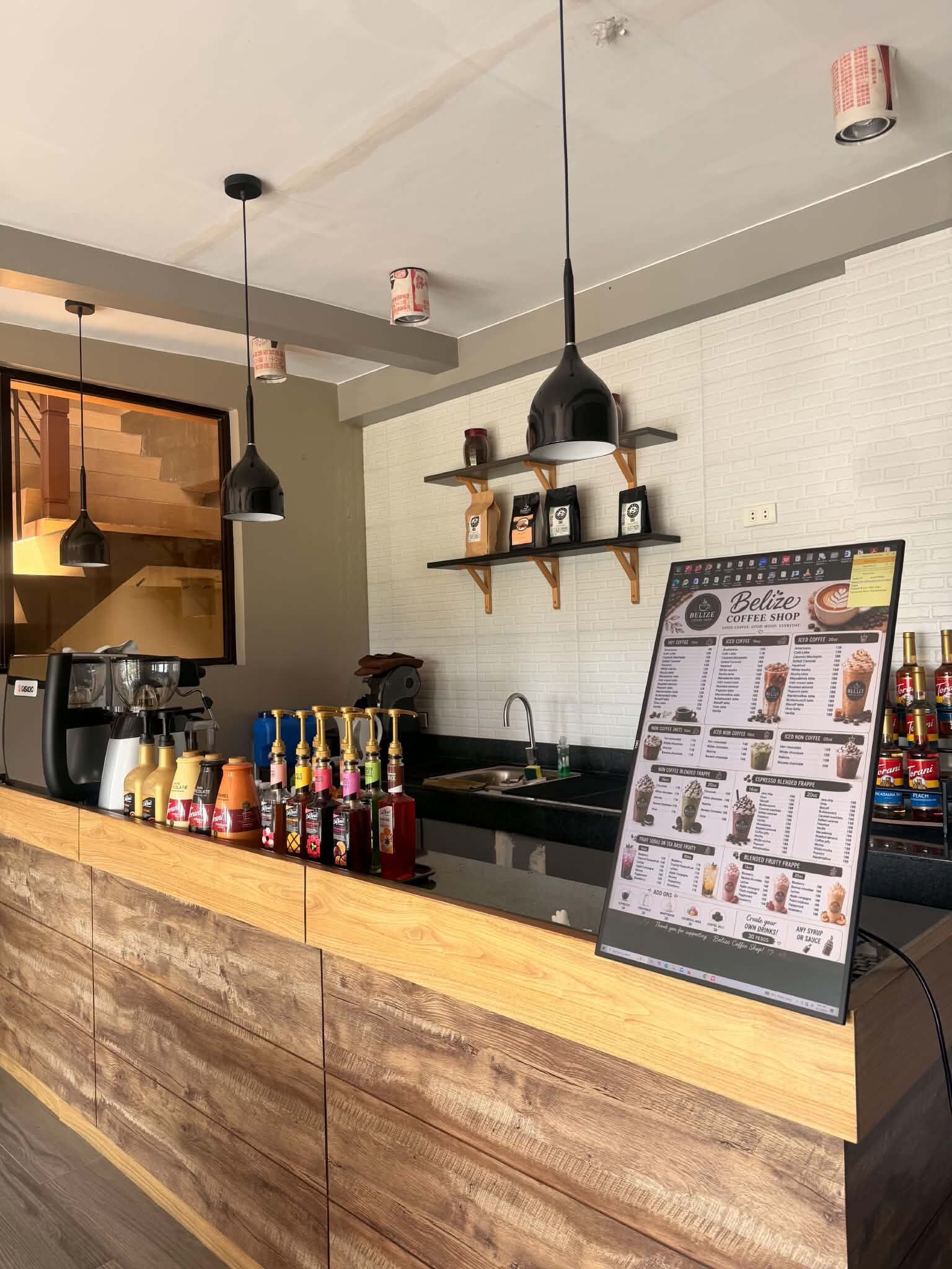 A coffee shop counter with a menu board, espresso machines, and a variety of coffee and tea bottles.