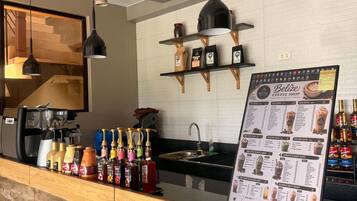 A coffee shop counter with a menu board, espresso machines, and a variety of coffee and tea bottles.