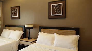 A hotel room with two beds, each with white bedding and headboards. There are two framed wall decorations above the beds and a lamp on a bedside table.